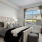 Model bedroom at our senior living community in Farmington, featuring carpeted flooring and windows with curtains.
